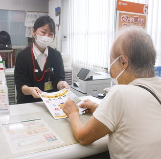 霧が丘郵便局の窓口で冊子を配布する職員