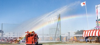 快晴の空の下で一斉放水。大きな虹が現れ、来場者から拍手が送られた