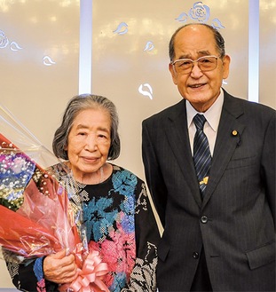 同会から贈られた花束を持つ洋子夫人と高橋さん(右)