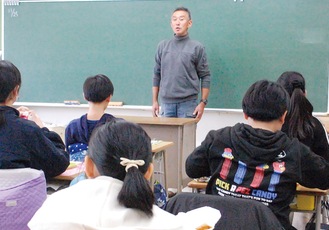 給食を食べる児童たちの前で話をする吉田さん