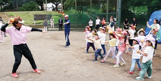 宇津木さん(左)の動きをマネして投げる動作を行う子どもたち