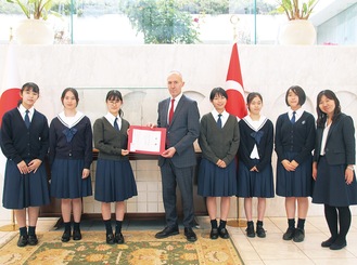 （左から）宮木瑠花さん、帆足凛生菜さん、小嶋夢叶さん、ジェミル・ウフック・トールル一等参事官、八木橋美悠さん、小川友楽さん、橋本茉和さん、佐々木未欧教諭＝5月26日、東京都渋谷区