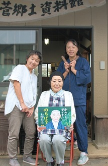 左から清水さん、紙芝居を持つ寛子さん、望月さん。高橋さんが生前、古農具などを展示するため自宅敷地内に設営した「菅郷土資料館」の前で＝10月４日