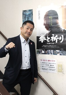 映画のポスターの前に立つ新田会長