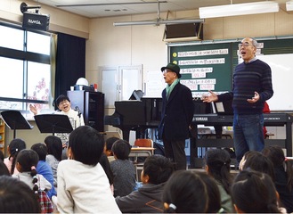 写真奥左から、児童と歌う丸山さんと平本さん、丸山さんの夫の哲郎さん