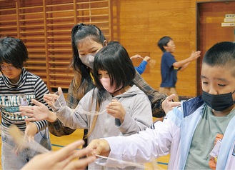 完成したぶんぶんごまを綺麗に回そうと教え合う児童ら