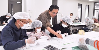 取り出した骨をイラストと照らし同定する名誉学芸員の高槻さん（左から３人目）