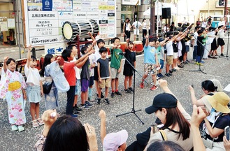 七夕まつりで完成した歌を披露する児童と一緒に拳を突き上げる来場者