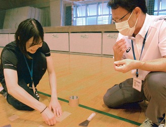 職員の指導を受けながら、体育館の床の保守作業をする原田さん（左）