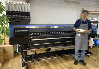 印刷機の前で特製カレーを手にする松井さん