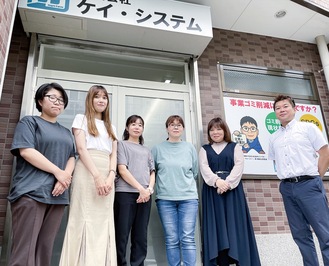 相模大塚駅前に移転した新しい事務所の前で。小島代表（右）が率いる同社では女性も多く活躍している