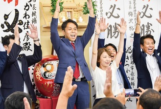 当選を決め、支持者らと万歳三唱で喜ぶ橘川氏（中央）、右は妻の志保さん。その右に綱嶋洋一県議　＝7月7日午後11時すぎ・橘川氏選挙事務所