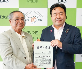 市長に冊子を手渡す田中代表（左）