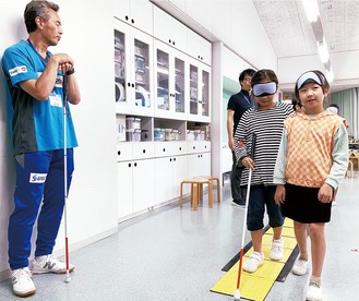パラリンピックメダリストの葭原さん（左）の指導で視覚障害者の生活を体験する児童ら