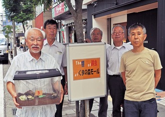 虫かごを抱える（左から）程嶋理事長と石井理事、商店街の会員ら