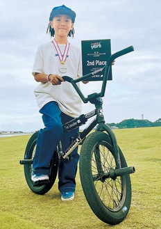 愛用する自転車に乗り、メダルと賞状を見せる尾後家選手