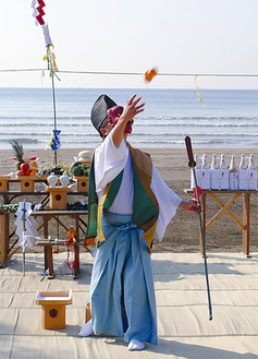 天狗の面をつけた神職がみかんを振舞う（今月11日、材木座海岸）