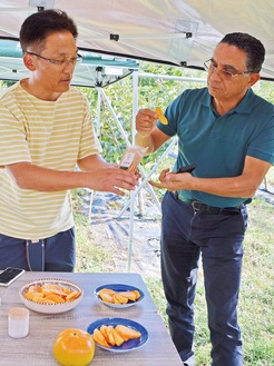 太秋のドライフルーツを試食するナセフさん（右）と説明する清水さん