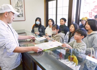 御菓子司「たかはし」の店主・高橋さんにクリマサリを広めるためのポスターとチラシを手渡す児童