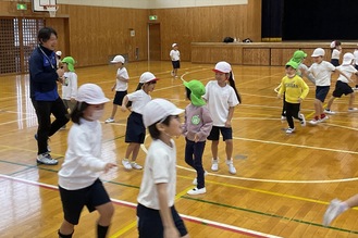 指導を行う飯田さん（左）とジャンケン鬼ごっこで準備運動するする子どもたち